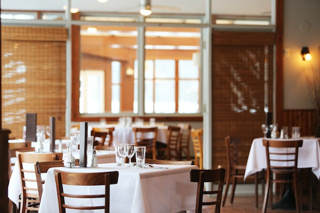 restaurant with white table cloths, square tables and set for a dinner rush